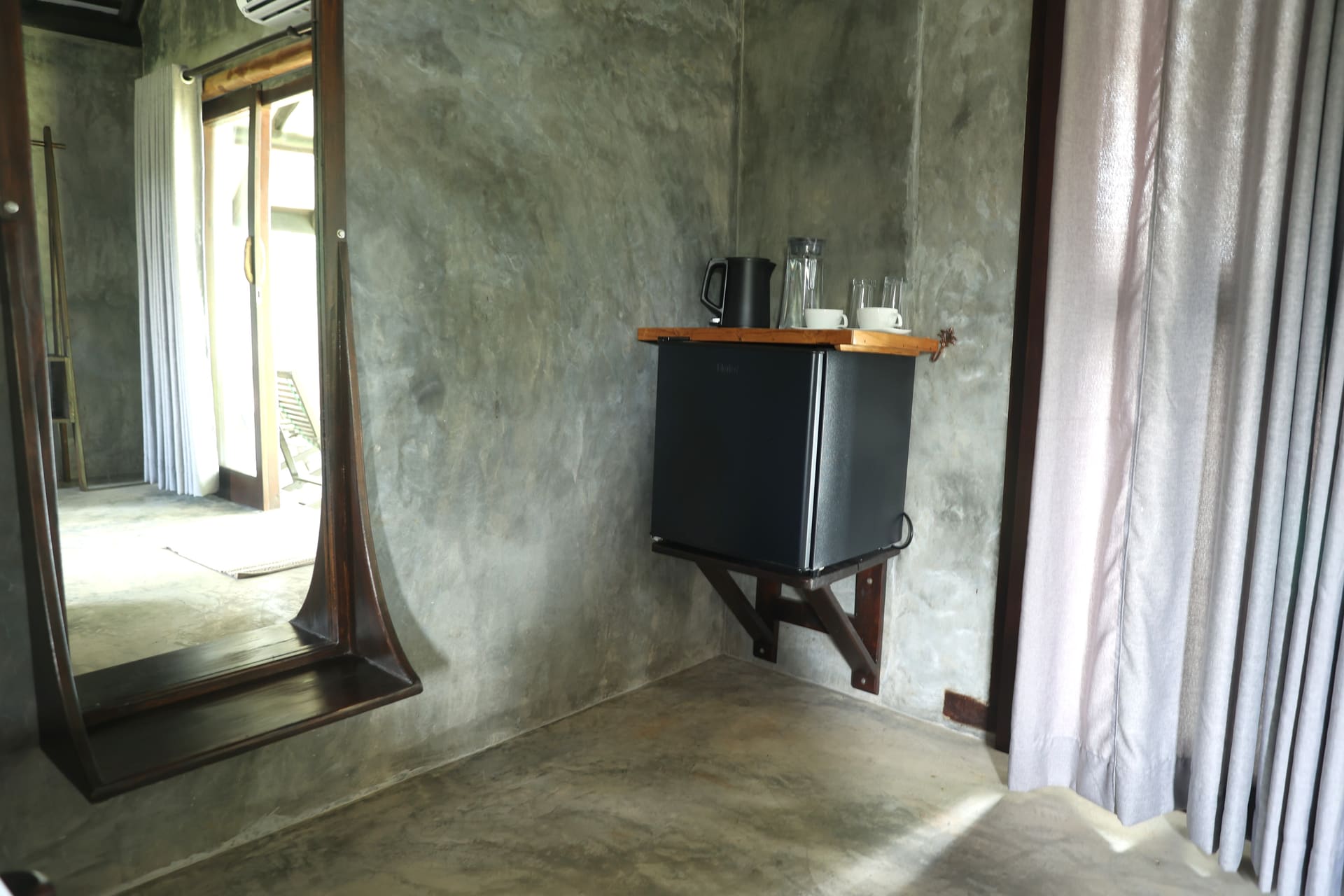 Mini fridge with kettle and glassware — raw concrete walls