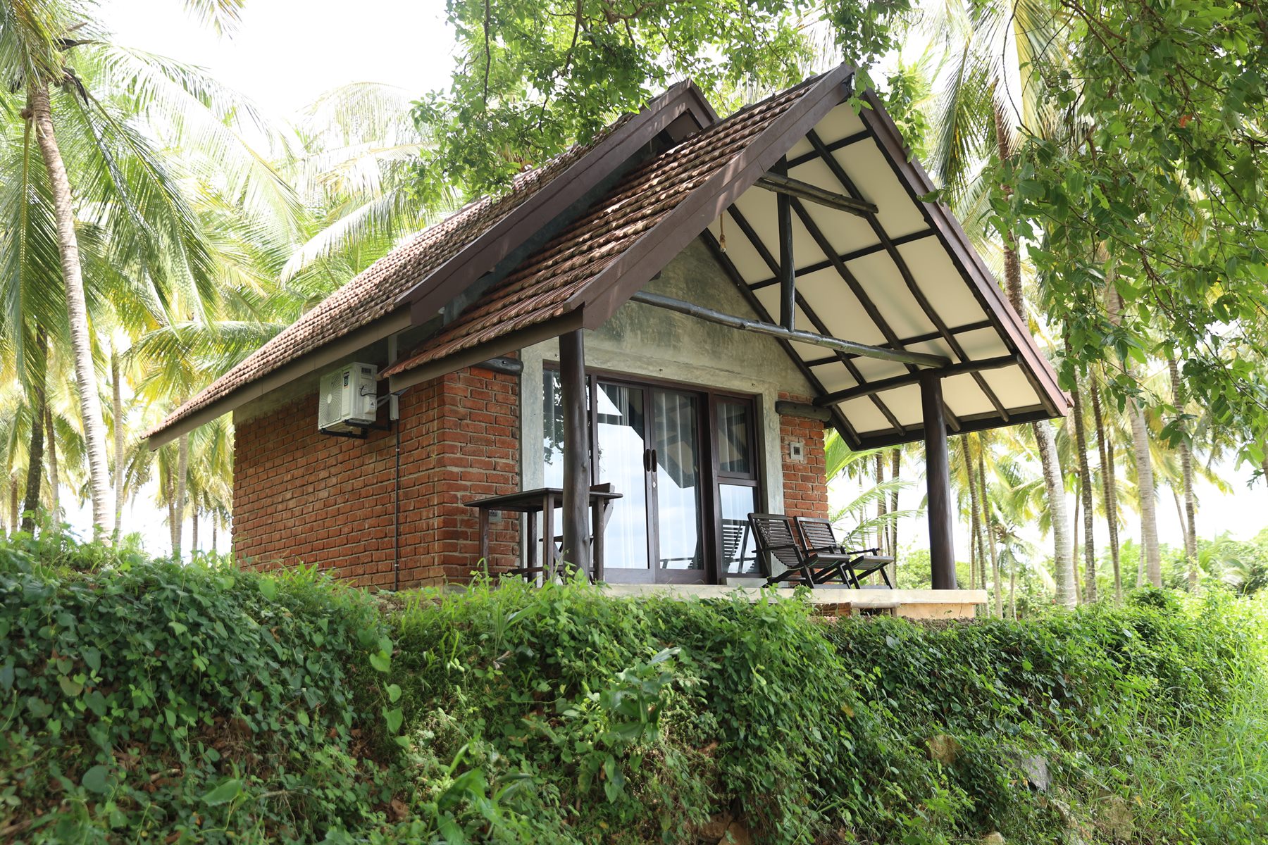 A brick cottage veranda tucked under palms and trees at Aji Fruit Farm
